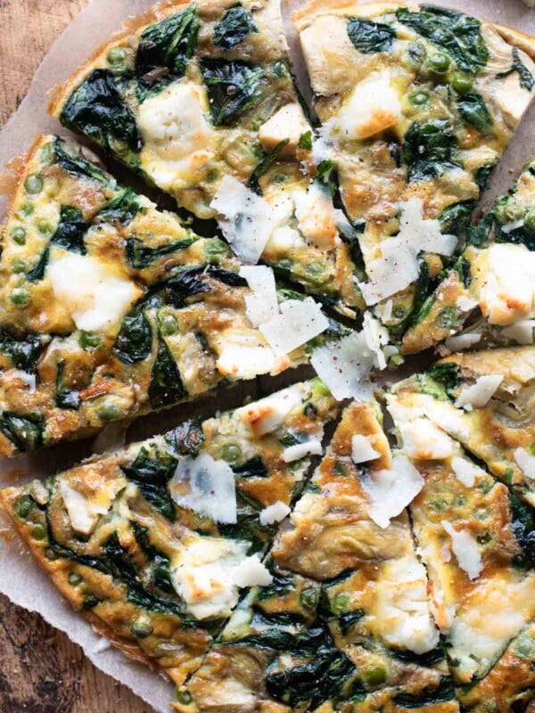 An overhead shot of a spinach and artichoke frittata cut into slices sitting on a wooden cutting board.