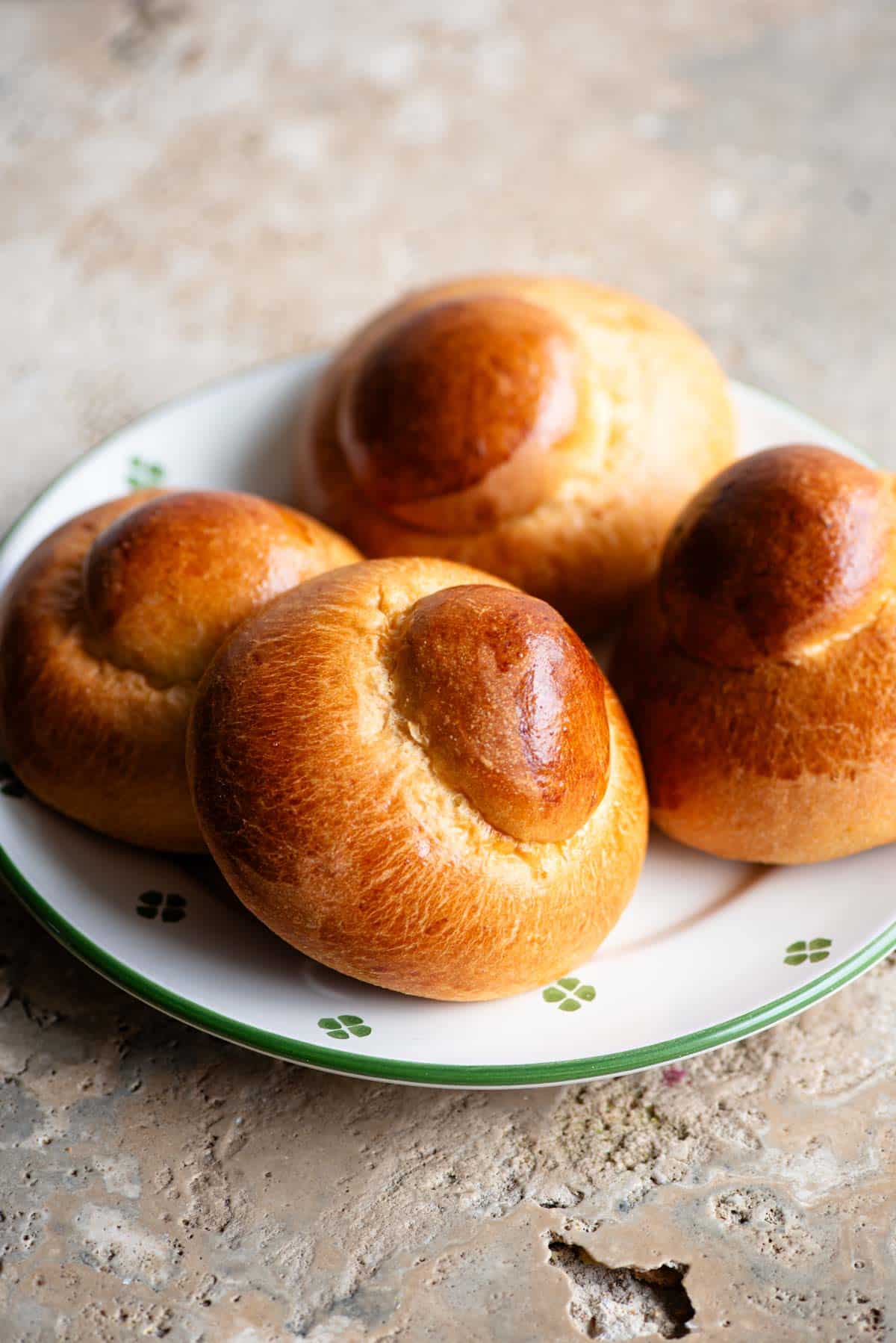 Four Sicilian brioche buns on a plate sitting on a travertine surface.